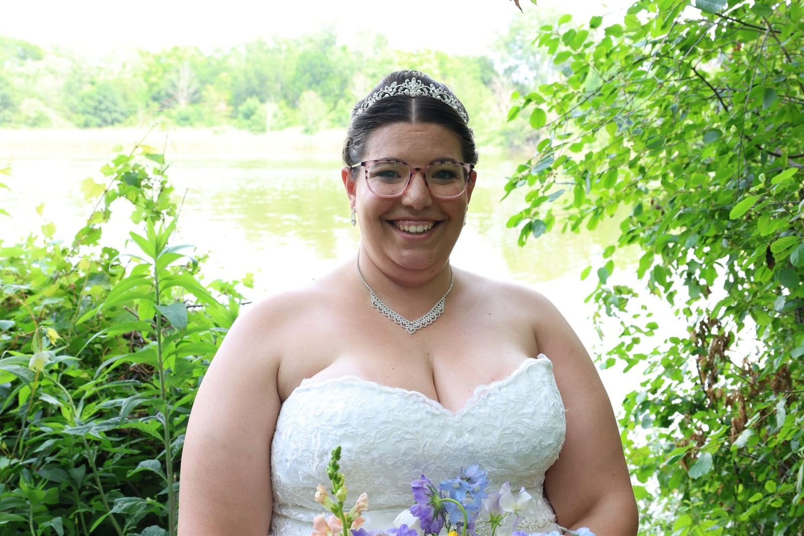 Smiling bride among green leaves by the water