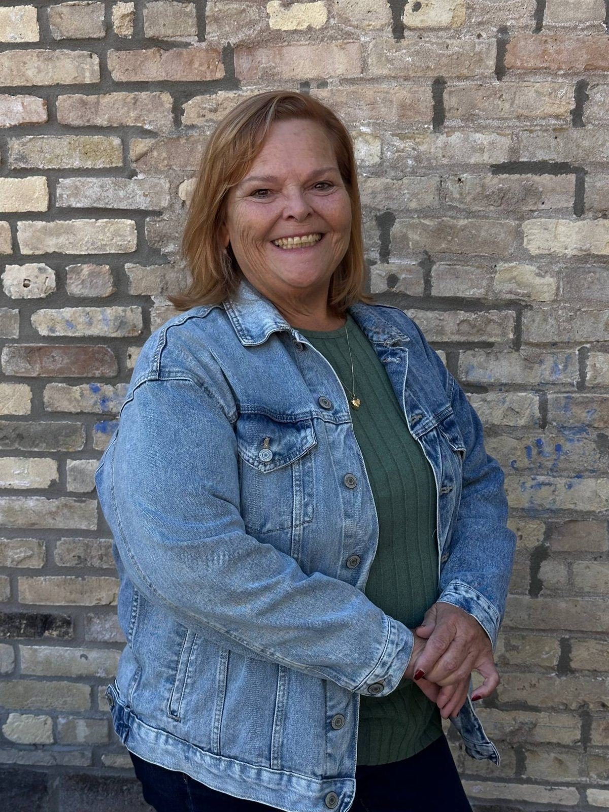 Heather smiling in a denim jacket in front of a brick wall